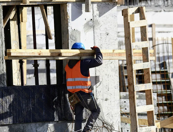 Construction worker carrying timber on a concrete building site